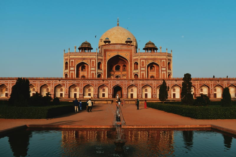Humayun's Tomb at golden hour — frontal-symmetrical with charbagh fountain and reflecting channel — the premium iconic Delhi composition